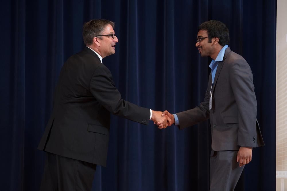 Doctor Smart shaking hands with an award recipeint in a grey suit